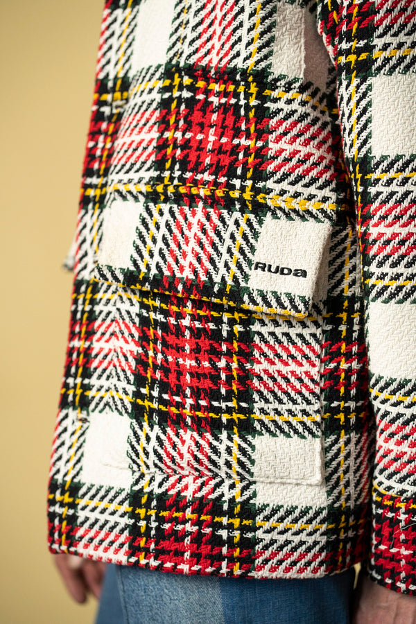 Close-up of a person wearing the Check Workers Jacket adorned with a red, white, black, and yellow plaid pattern. The jacket features prominent stitching and a visible front pocket embroidered with the Ruda Patrice brand name. The person is also wearing blue jeans.